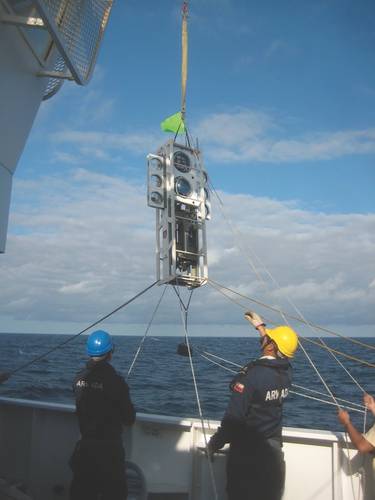 Figure 2: The benthic lander Audacia is raised over the side for deployment by the deck crew of the modern Chilean scientific vessel Cabo de Hornos, operated by the Chilean Armada.  The glass spheres put bouyancy high, while the instruments put the weight low, creating inherent stability. (Image: Courtesy Kevin Hardy and Atacamex 2018)
